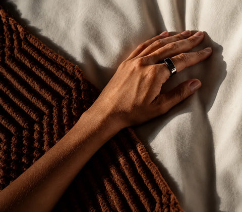 Oura Ring 4 worn on a person’s finger while resting on a bed | SmartRing Philippines