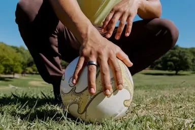 Person in sportswear gripping a soccer ball on grassy field, outdoors in a park. | Smartring PH